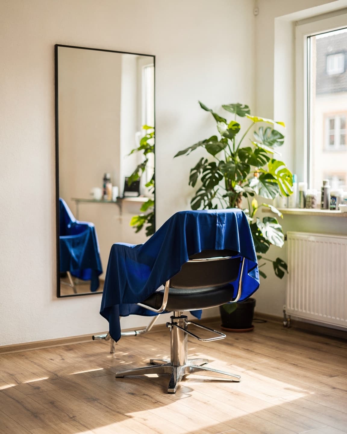 Salonstuhl mit blauem Umhang vor dem Spiegel im hellen Tageslicht