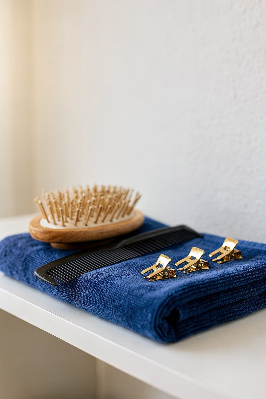 Runde Holzbürste, Kamm und goldene Haarclips auf blauem Frottee