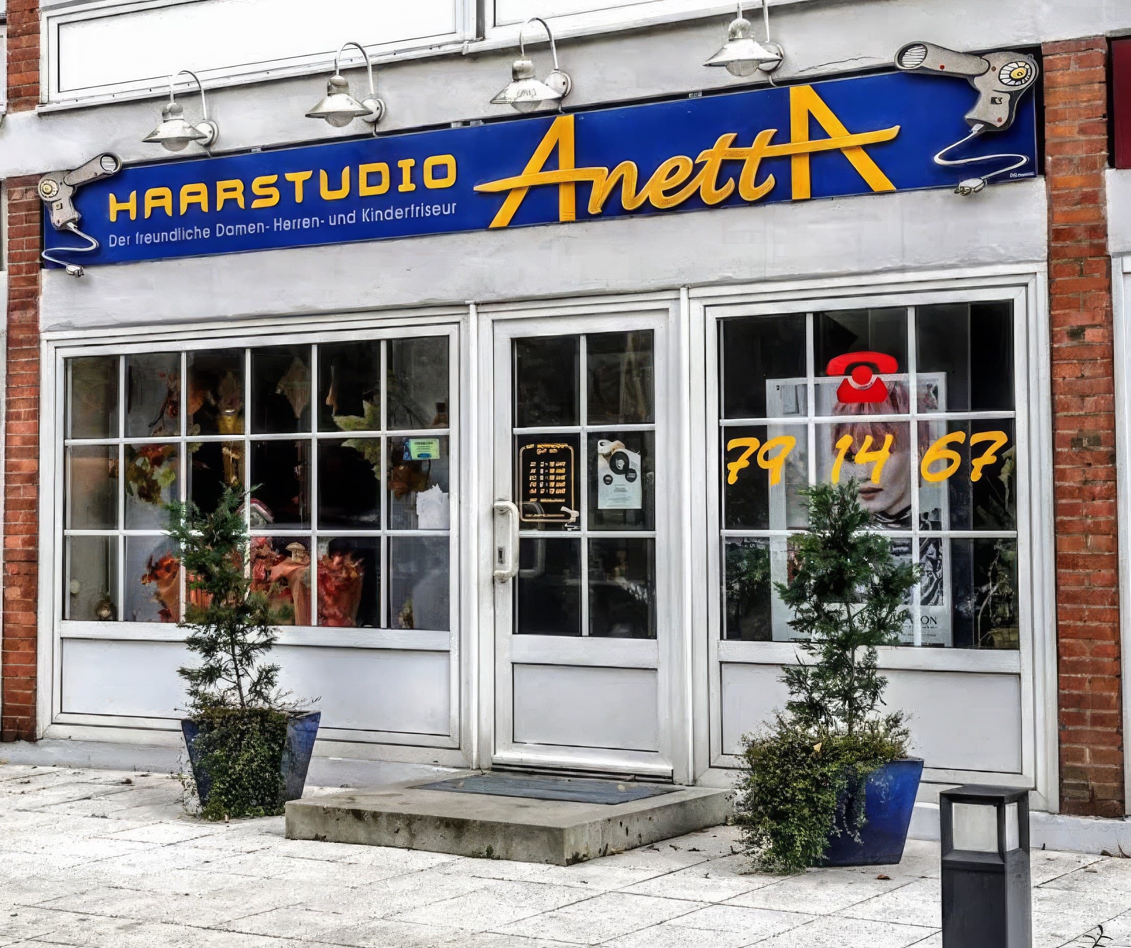 Die Ladenfront des Haarstudio Anetta: blaues Schild mit gelbem AnettA-Schriftzug über den Schaufenstern